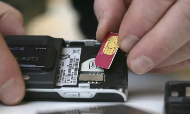 Händer sätter i ett oregistrerat kontantkort i en äldre mobiltelefon.