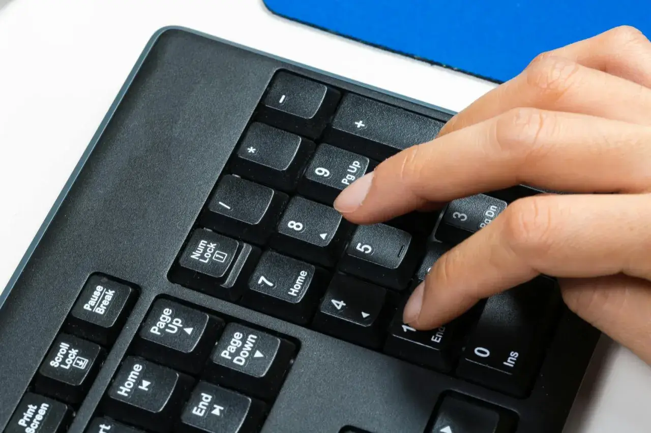 En hand trycker på siffertangenten 5 på ett numeriskt tangentbord. Kanske för att skriva in ett snabel a i ett mejl.