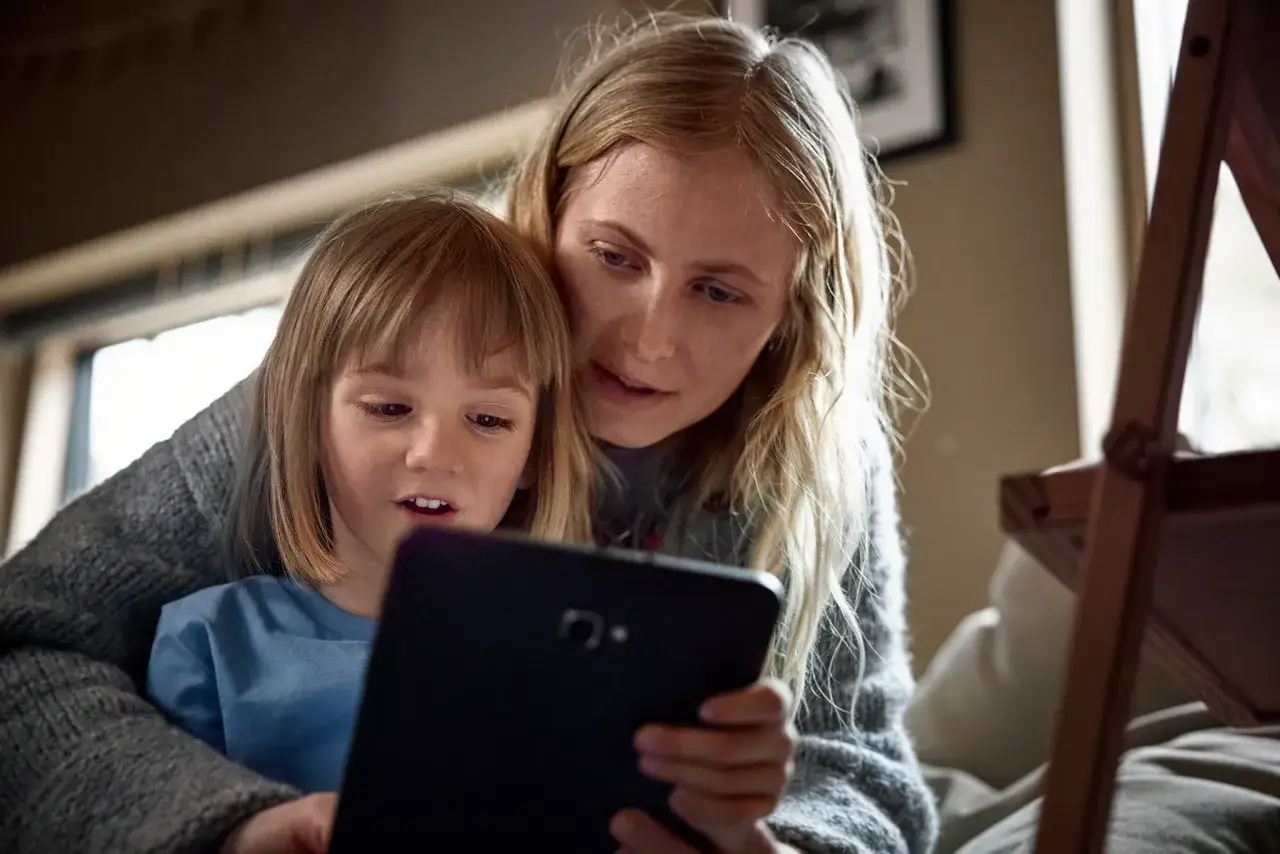 Kvinna och barn tittar p&aring; en surfplatta, kanske p&aring; sociala medier. Barnet &auml;r i f&ouml;rgrunden, kvinnan bakom.