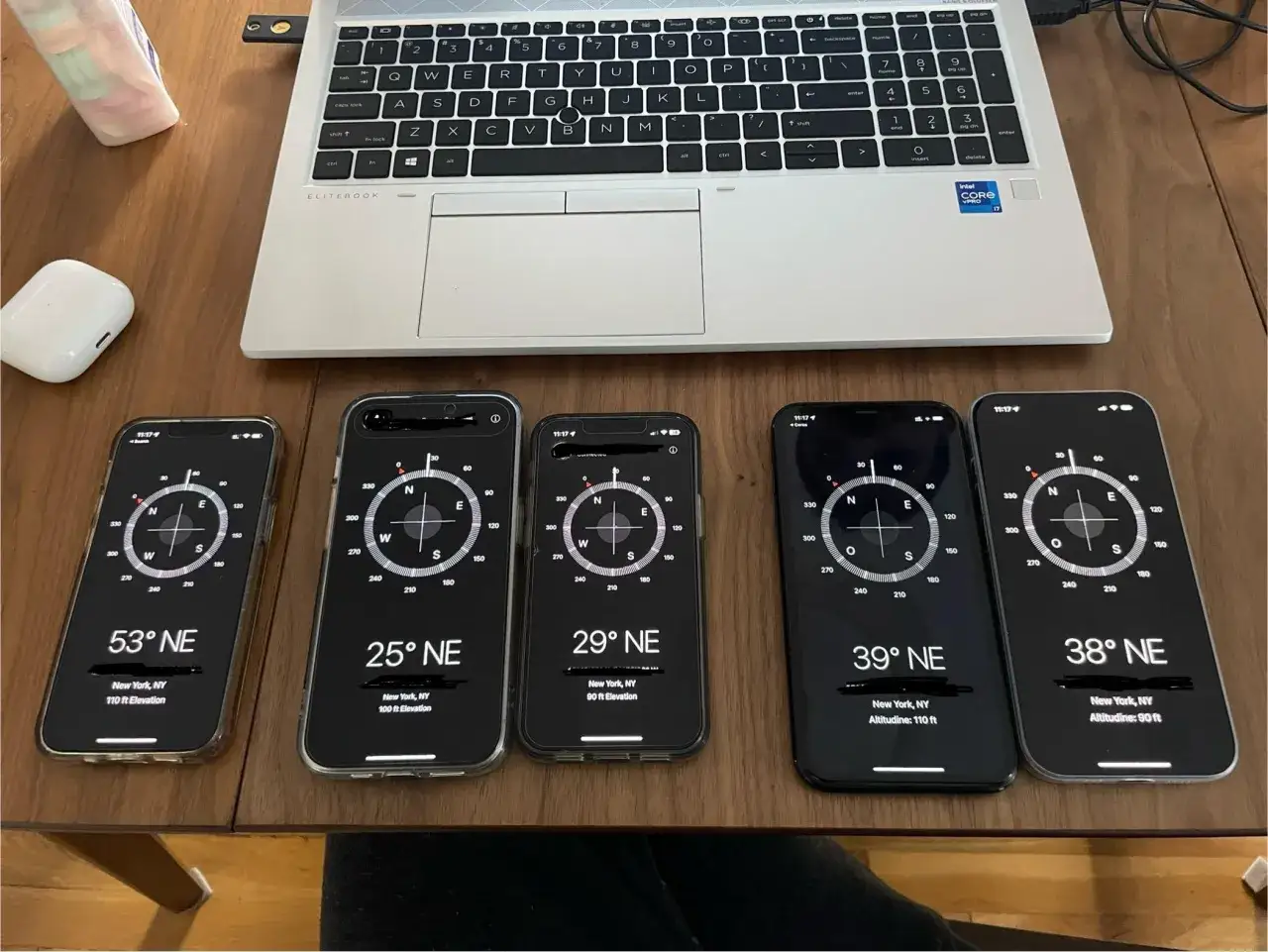 Fem iPhones visar en kompass i mobilen. En laptop och AirPods ligger bredvid.