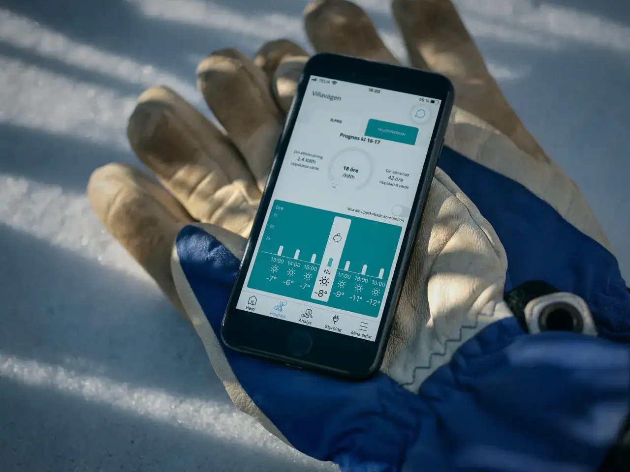 En mobiltelefon visar elpriser och prognoser i elpriskollen appen, placerad p&aring; en handske i sn&ouml;n.