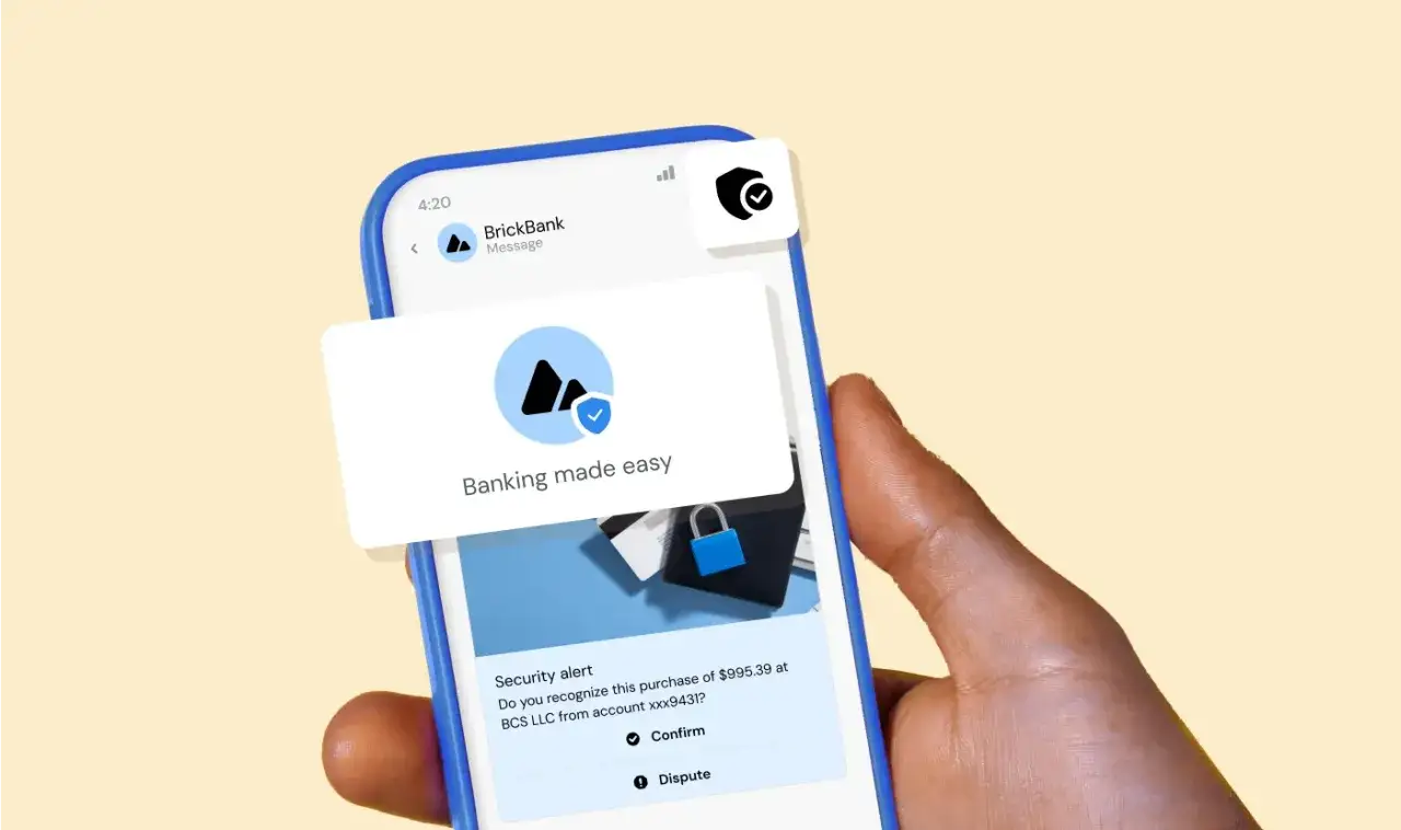 En hand håller en mobil med ett rcs meddelande från BrickBank. Meddelandet varnar för ett köp och erbjuder bekräftelse eller tvist.