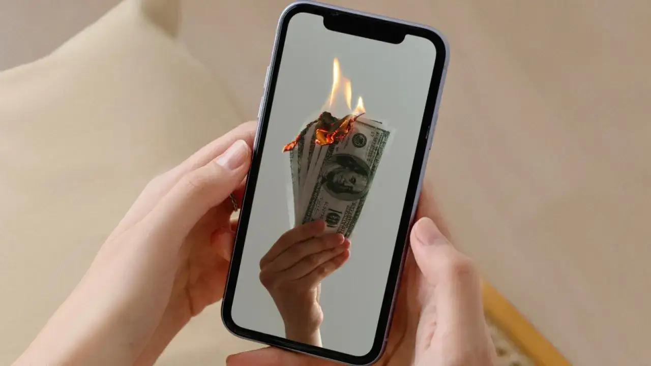 En mobil visar en hand som håller sedlar som brinner. Kanske en bild av en misslyckad apple återbetalning.