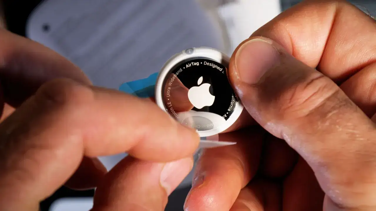 Händer som hanterar en Apple AirTag, redo att sättas i bruk. Lång airtag batteritid ger trygghet.